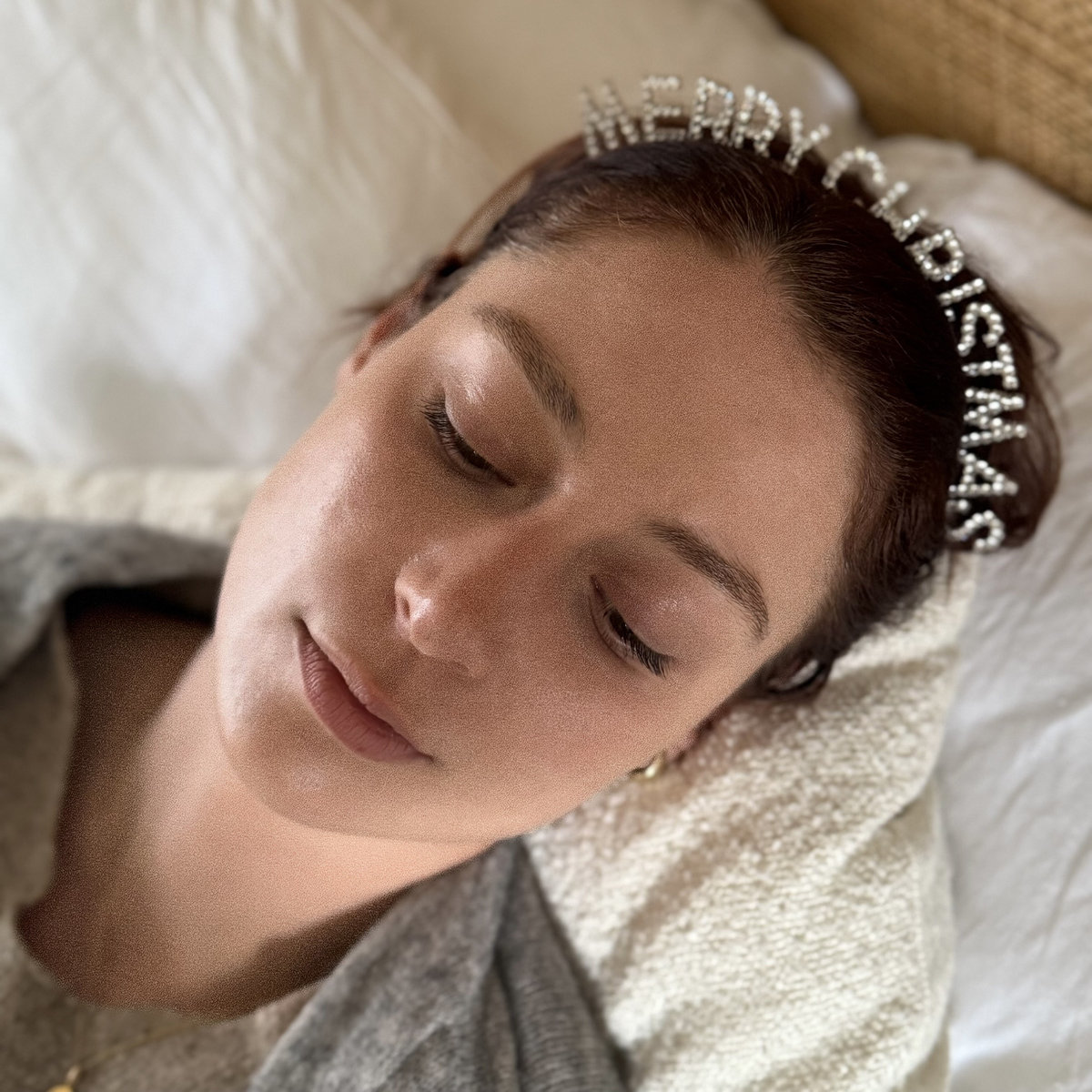 A woman laying on a pillow, with the shot of her face, eyes closed, wearing a "Merry Christmas" headband.