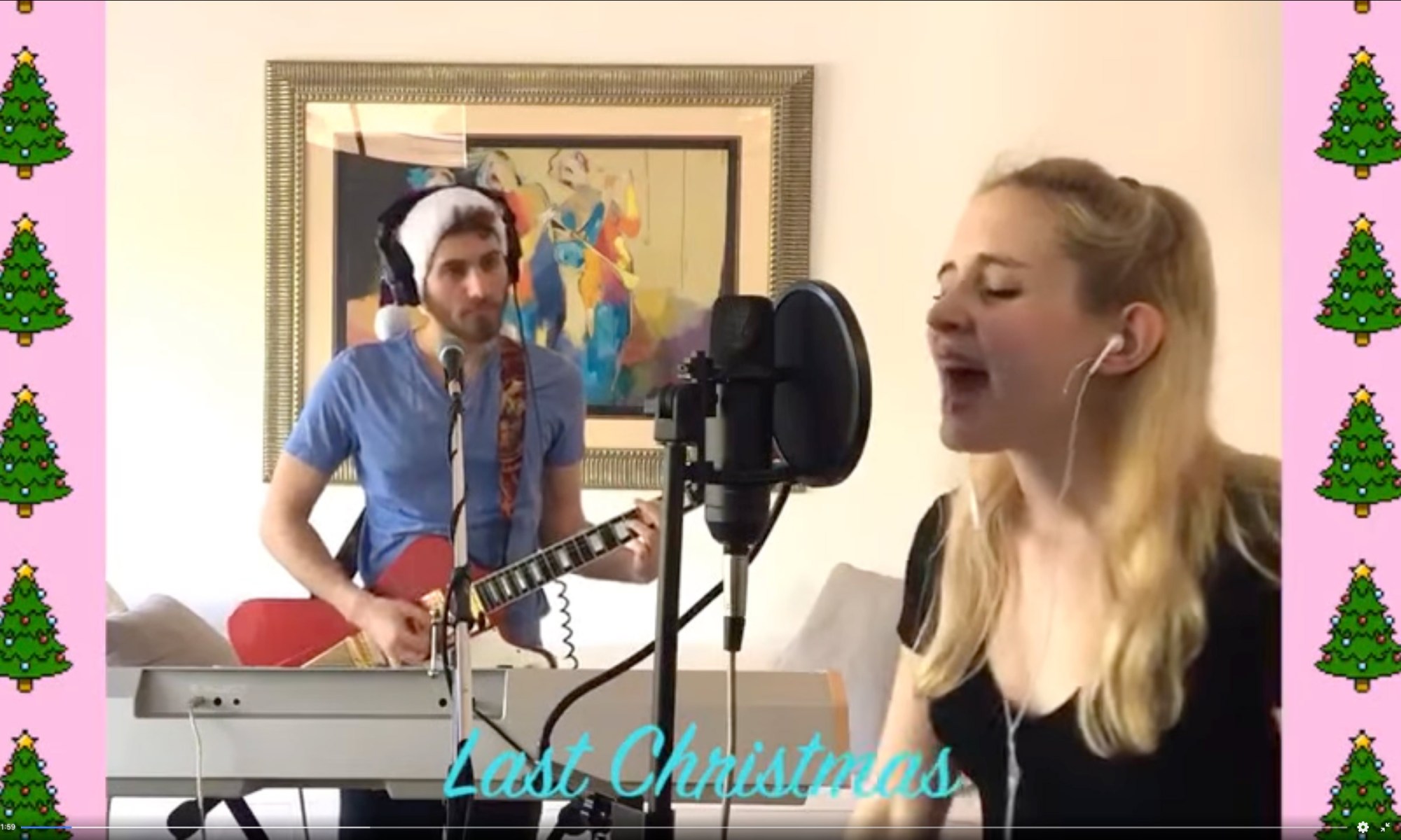girl singing into a microphone while a guy stands in the background playing guitar while wearing a santa hat