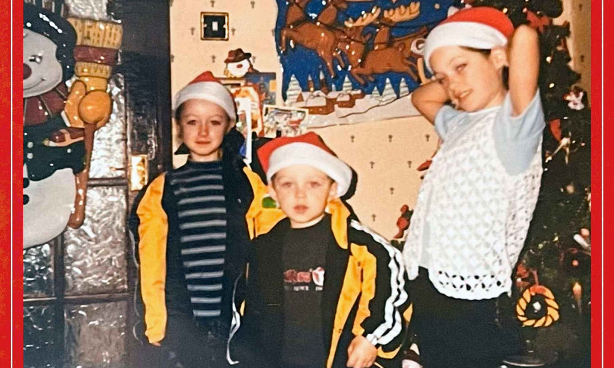 A christmas scene with three young boys wearing santa hats in front of a tree.