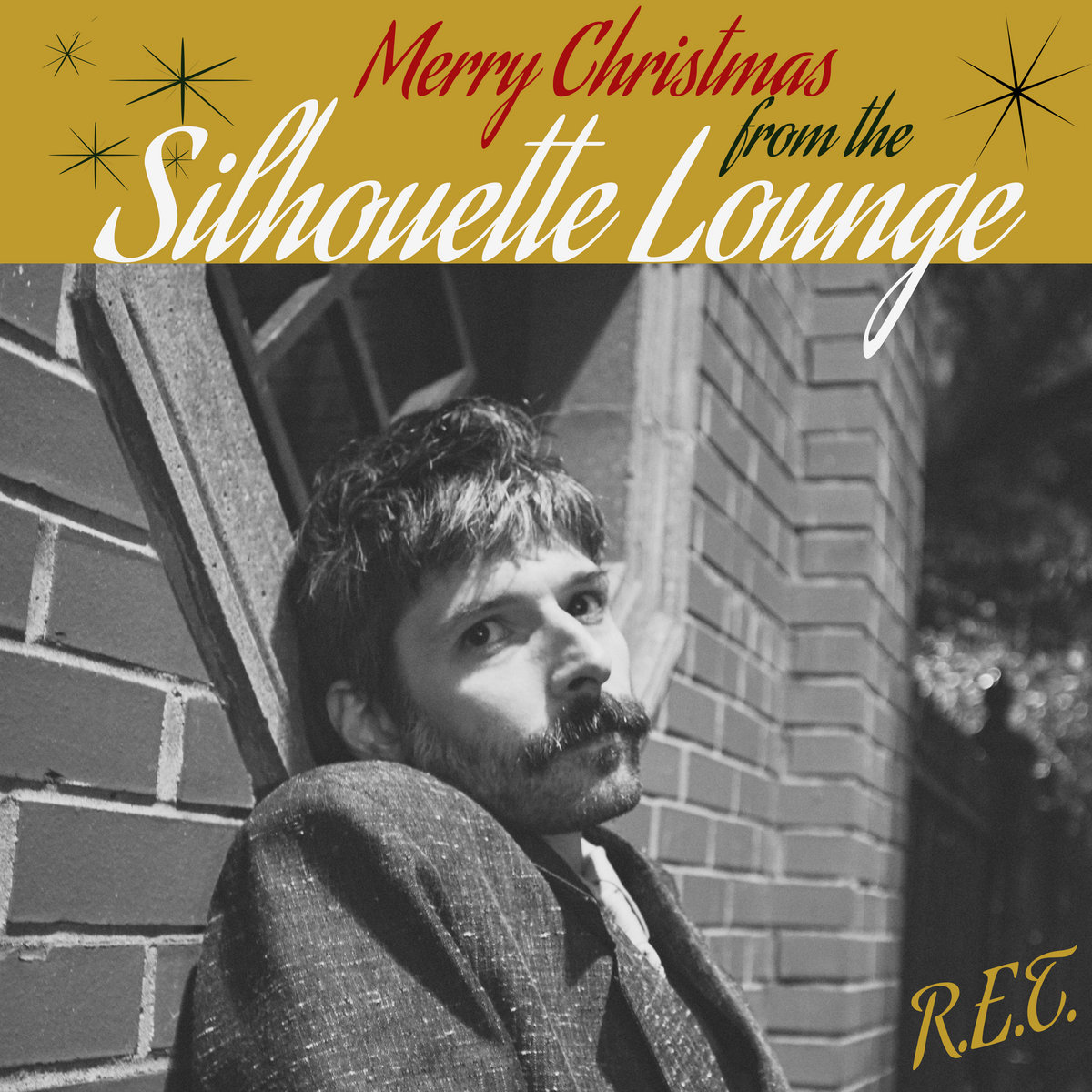 A man with short hair and a beard is leaning against a brick wall. The title of the song "Merry Christmas from the Silhouette Lounge" is above him, and his initials, "R.E.T." is written in the bottom right corner.